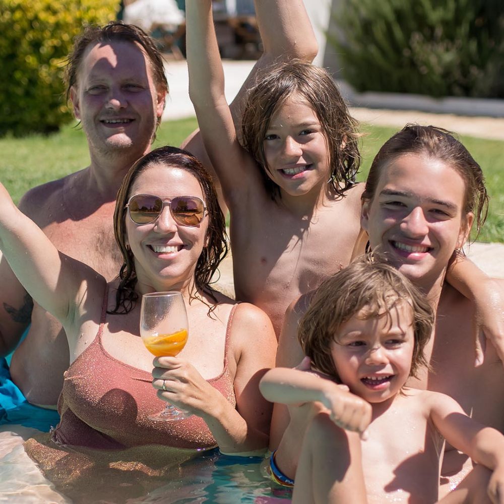 funny-family-swimming-pool-backyard-cute-boys-different-ages-mid-adult-parents-looking-camera-smiling-rising-hands-leisure-family-party-concept